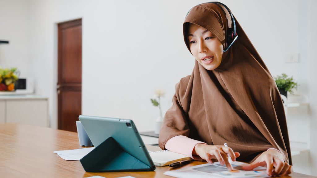 muslim lady wear headphone using digital tablet talk colleagues about sale report conference video call while working from home kitchen